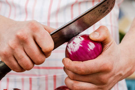 A male cook peels onions with a knife in close-up. The concept of organic cooking.
