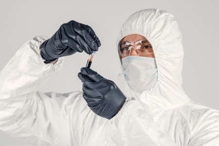 A test tube in a man's hand close-up , a man in a medical mask holding a bottle of red liquid....