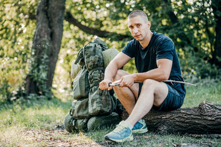 A man with a knife cut a wooden stick for a fire in the woods. The concept of tourism, hunting and peopleの写真素材