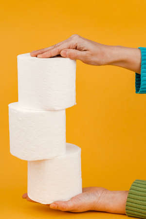 A roll of toilet paper in a woman's hand on a yellow background.