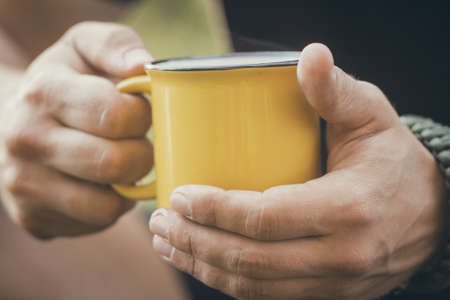 Man traveler hands holding a Cup of tea outdoors. The concept of adventure, travel, tourism and camping. Tourist drinking tea from a mug in the camp.の写真素材