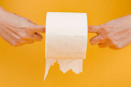A roll of toilet paper in a woman's hand on a yellow background.の写真素材