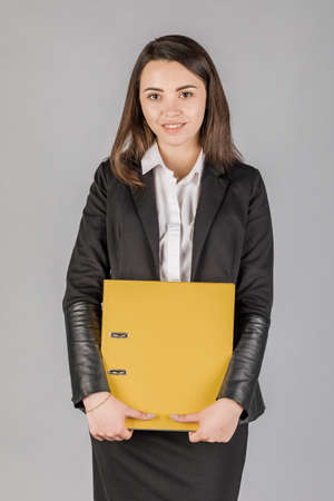 Young business woman in dark suite with file on grey background. Office conceptの写真素材