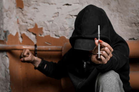 The concept of drug dependence and withdrawal symptoms. A depressed and hopeless teenage girl holds a syringe with drugs in her hand.の写真素材