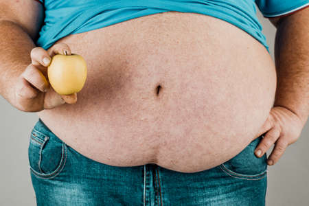 The fat man holds a Apple in front of his bare stomach. The concept of diet and healthy eating.の写真素材