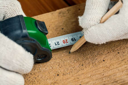 A carpenter with a pencil and tape measure measures a wooden Board on the table.