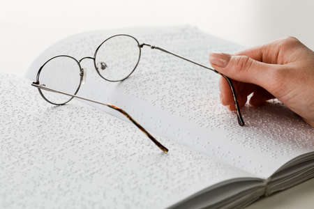 A woman holds black-rimmed glasses against the background of an open textbook reading books in Braille.の写真素材
