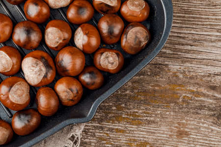 Roasted chestnuts served in a special perforated chestnut pan on an wooden tableの写真素材