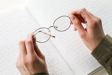 A woman holds black-rimmed glasses against the background of an open textbook reading books in Braille.の写真素材