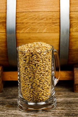 A glass of wheat or malt next to a wooden barrel