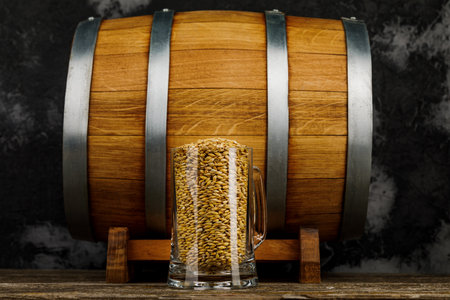 A glass of wheat or malt next to a wooden barrelの写真素材