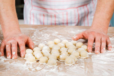 A man prepares and shapes small homemade raw dumplings with meat on the kitchen table. Do it yourselfの写真素材