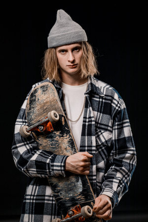 Portrait of a stylish man holding a skateboard in the Studio. Close-up of a smiling skateboarder...