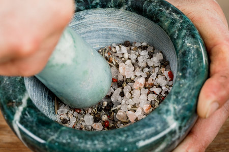 A male chef grinds spices and herbs in a cooking mortar.