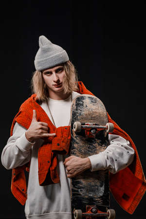 Portrait of a stylish man holding a skateboard in the Studio. Close-up of a smiling skateboarder posing on a black background.の写真素材