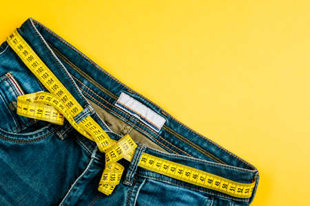The concept of a healthy lifestyle and diet. Blue jeans with a yellow measuring tape instead of a belt.の写真素材