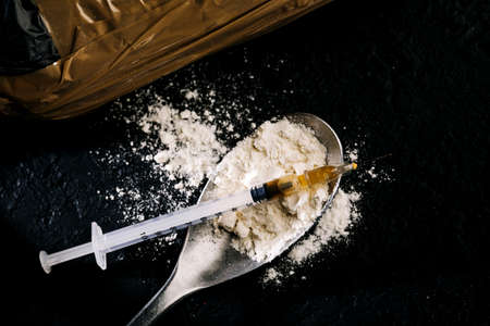 Heroin in a syringe and heroin powder on a black background. the concept of a narcotic substance.の写真素材