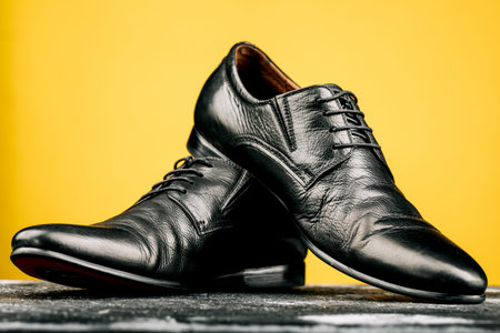 Men's accessories with black leather shoes on a wooden table, bar or counter on a yellow wall backgroundの写真素材