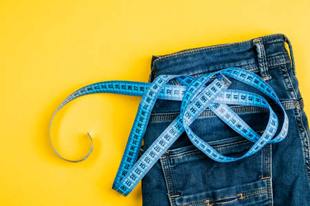 The concept of a healthy lifestyle and diet. Blue jeans with a blue measuring tape instead of a belt.の写真素材