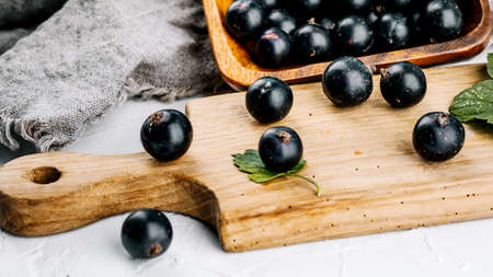 Black currant on a wooden board on a white concrete table.の写真素材