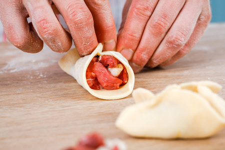 A man is holding a khinkali in close-up. Cook in the kitchen. The process of preparing a national dishの写真素材