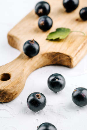 Black currant on a wooden board on a white concrete table.の写真素材