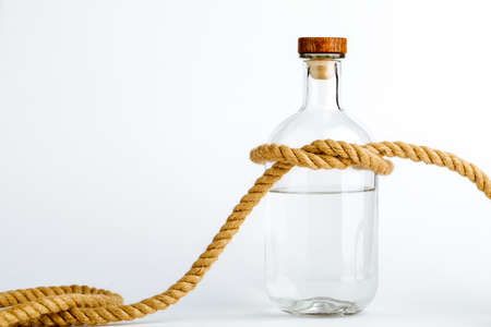 A glass bottle with alcohol tied in a rope knot, the concept of the treatment of alcoholism.の写真素材