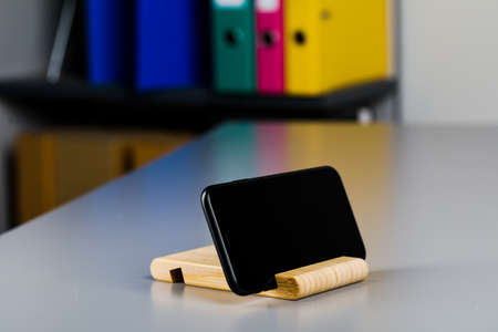 A black smartphone on a wooden stand is lying on the table. A place to copy.の写真素材