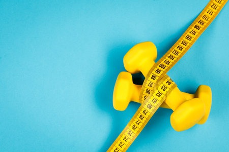 Yellow dumbbells and measuring tape on a blue background with a place to copyの写真素材