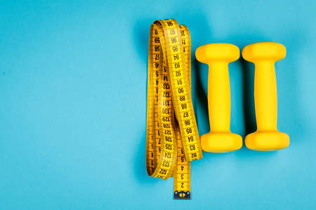 Yellow dumbbells and measuring tape on a blue background with a place to copyの写真素材