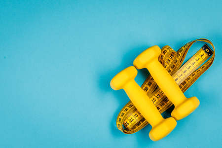 Yellow dumbbells and measuring tape on a blue background with a place to copyの写真素材