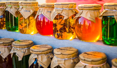 Jars with honey and jam standing on rack. Some with branch in it, in lights, multicolor, fermers festivalのeditorial素材