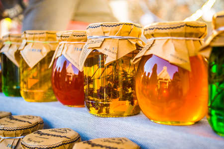 Jars with honey and jam standing on rack. Some with branch in it, in lights, multicolor, fermers festivalのeditorial素材