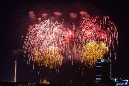 Beautiful colorful multicolor abstract firework or salute on the night black sky background, city with buildings on background. Celebration, New Year and anniversary concept.の写真素材