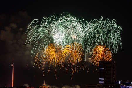 Beautiful colorful multicolor abstract firework or salute on the night black sky background, city with buildings on background. Celebration, New Year and anniversary concept.の写真素材