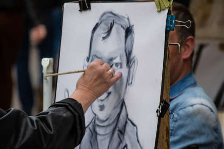 Street painter artist draws a cheerful portrait caricature of a man, hand with pencil on the paper, focus on portrait.の写真素材