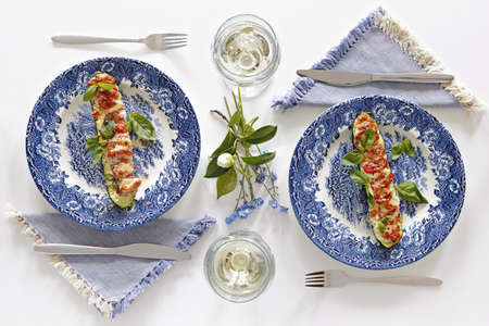Plates with baked courgette with tomatoes and cheese, glasses with white wine, romantic dinner for two. Homey atmosphere clean white table. Top viewの写真素材