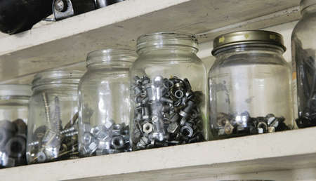 Various vintage old jars with metal bolts, nuts and screws on wooden cupboard in workshop. Closeupの写真素材