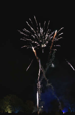 Shiny natural fireworks on dark black sky background with a little smoke. People silhouettes below.