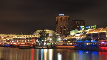 SINGAPORE - MARCH 02: Night shot of Clarke Quay at late evening and night over river in Singapore. Illuminated building of popular meeting place. At left side in background are hotels. In restaurants at promenade are many people.のeditorial素材