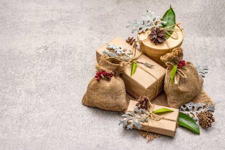 Christmas zero waste concept. New Year eco friendly packaging. Festive boxes in craft paper and sacks with different organic decorations. Stone concrete background, copy spaceの写真素材