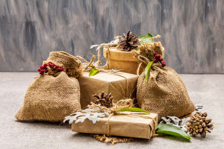 Christmas zero waste concept. New Year eco friendly packaging. Festive boxes in craft paper and sacks with different organic decorations. Stone concrete background, copy spaceの写真素材