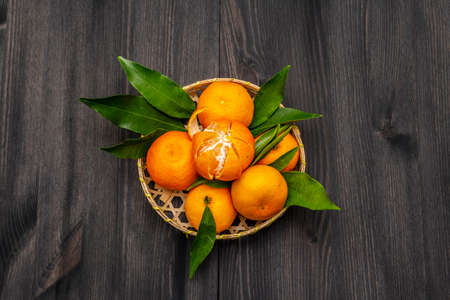 Fresh ripe tangerines with leaves in basket. New Year or Christmas wooden background. Festive good mood concept, copy space, top viewの写真素材