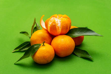Ripe tangerines with leaves. Fresh fruits isolated on green background, close upの写真素材