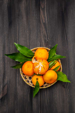 Fresh ripe tangerines with leaves in basket. New Year or Christmas wooden background. Festive good mood concept, copy space, top viewの写真素材