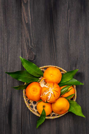 Fresh ripe tangerines with leaves in basket. New Year or Christmas wooden background. Festive good mood concept, copy space, top viewの写真素材