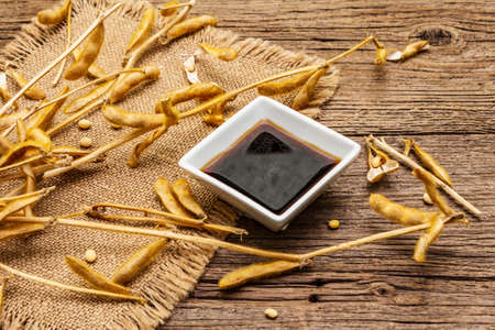 Ripe dry soybeans in pods and dark soy sauce. Cultivated organic agricultural crop, traditional healthy ingredients in oriental food. Vintage sackcloth, wooden boards background, close upの写真素材