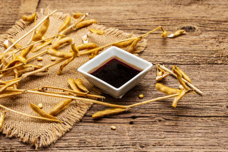 Ripe dry soybeans in pods and dark soy sauce. Cultivated organic agricultural crop, traditional healthy ingredients in oriental food. Vintage sackcloth, wooden boards background, close upの写真素材