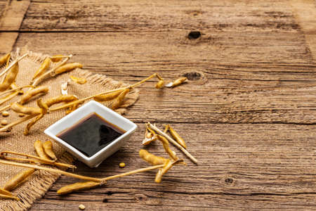Ripe dry soybeans in pods and dark soy sauce. Cultivated organic agricultural crop, traditional healthy ingredients in oriental food. Vintage sackcloth, wooden boards background, copy spaceの写真素材