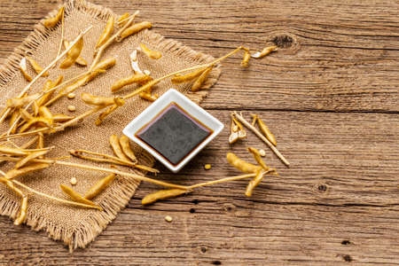 Ripe dry soybeans in pods and dark soy sauce. Cultivated organic agricultural crop, traditional healthy ingredients in oriental food. Vintage sackcloth, wooden boards background, copy spaceの写真素材